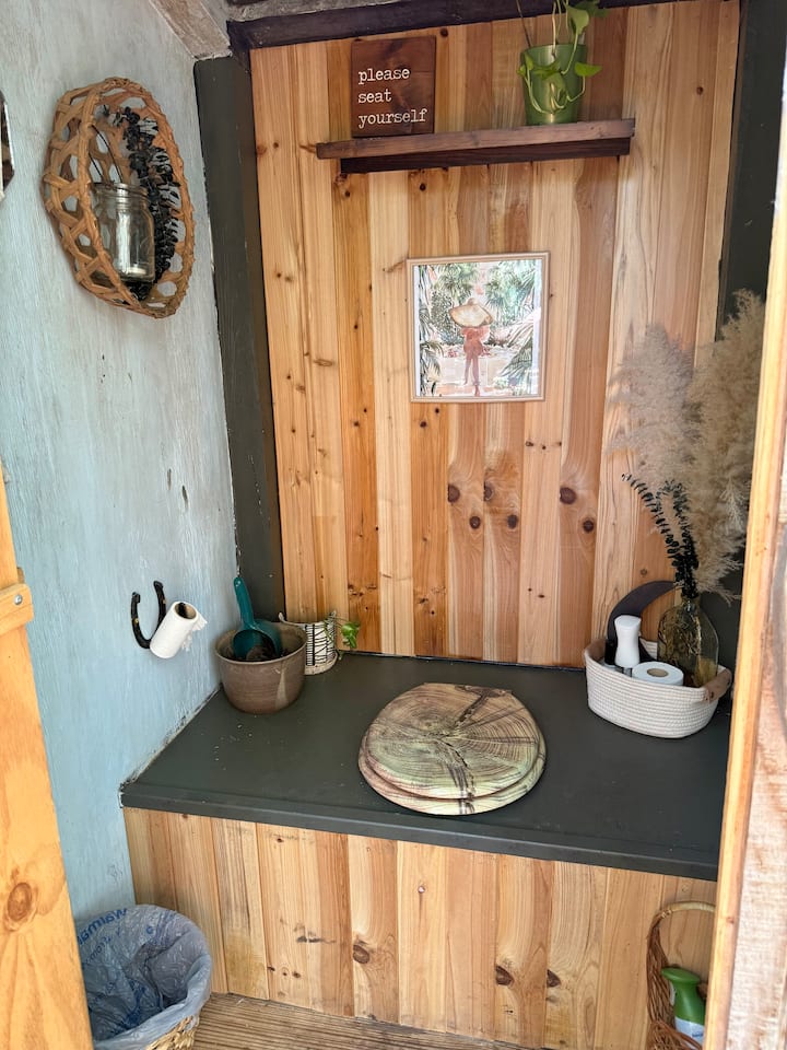 Composting outhouse with wooden walls and a please seat yourself sign