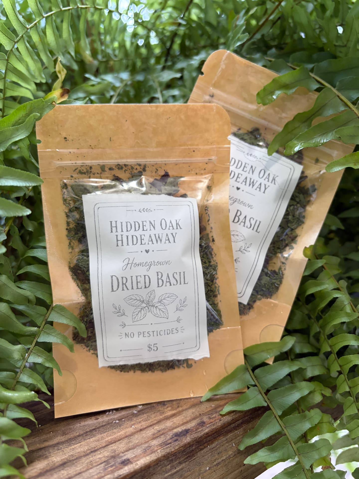 Two kraft pouches of Hidden Oak Hideaway homegrown dried basil among ferns